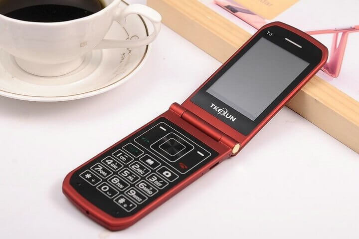 Teléfono Artfone de color rojo con la tapa desplegada rodeado de una taza de café. 
