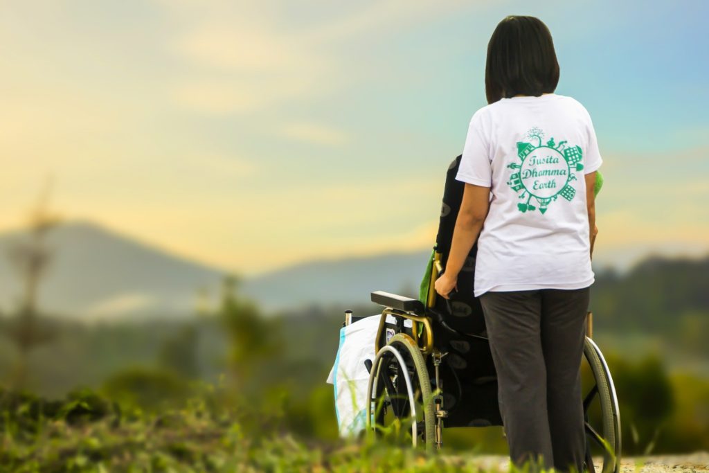 Enfermera cuidadora de mayores paseando una persona mayor en una silla de ruedas. 