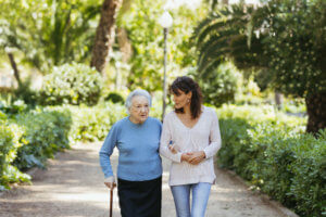 abuela con bastón caminando con la ayuda de una cuidadora