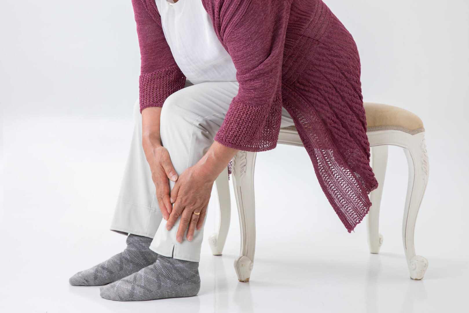 Un plano tres cuartos de una mujer mayor sentada se toca la parte de la espinilla de la pierna en claro gesto de dolencia. 