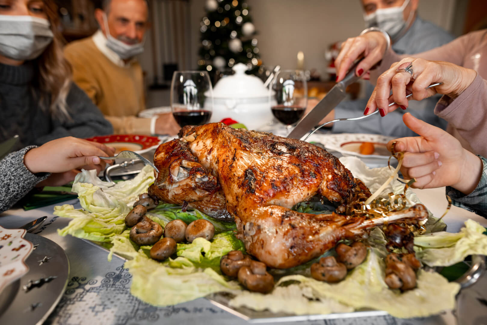 En la imagen, una familia se sitúa en la mesa mientras se parte con un chuchillo el pollo de la cena de Navidad, todos ellos portan la mascarilla para evitar el contagio del Covid en Navidad.