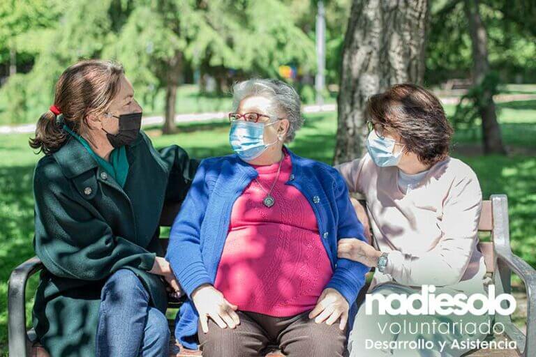 En la imagen se muestran dos personas jóvenes hablando con una señora mayor en un banco de un parque en un claro ejemplo que socializar no entiende de edad