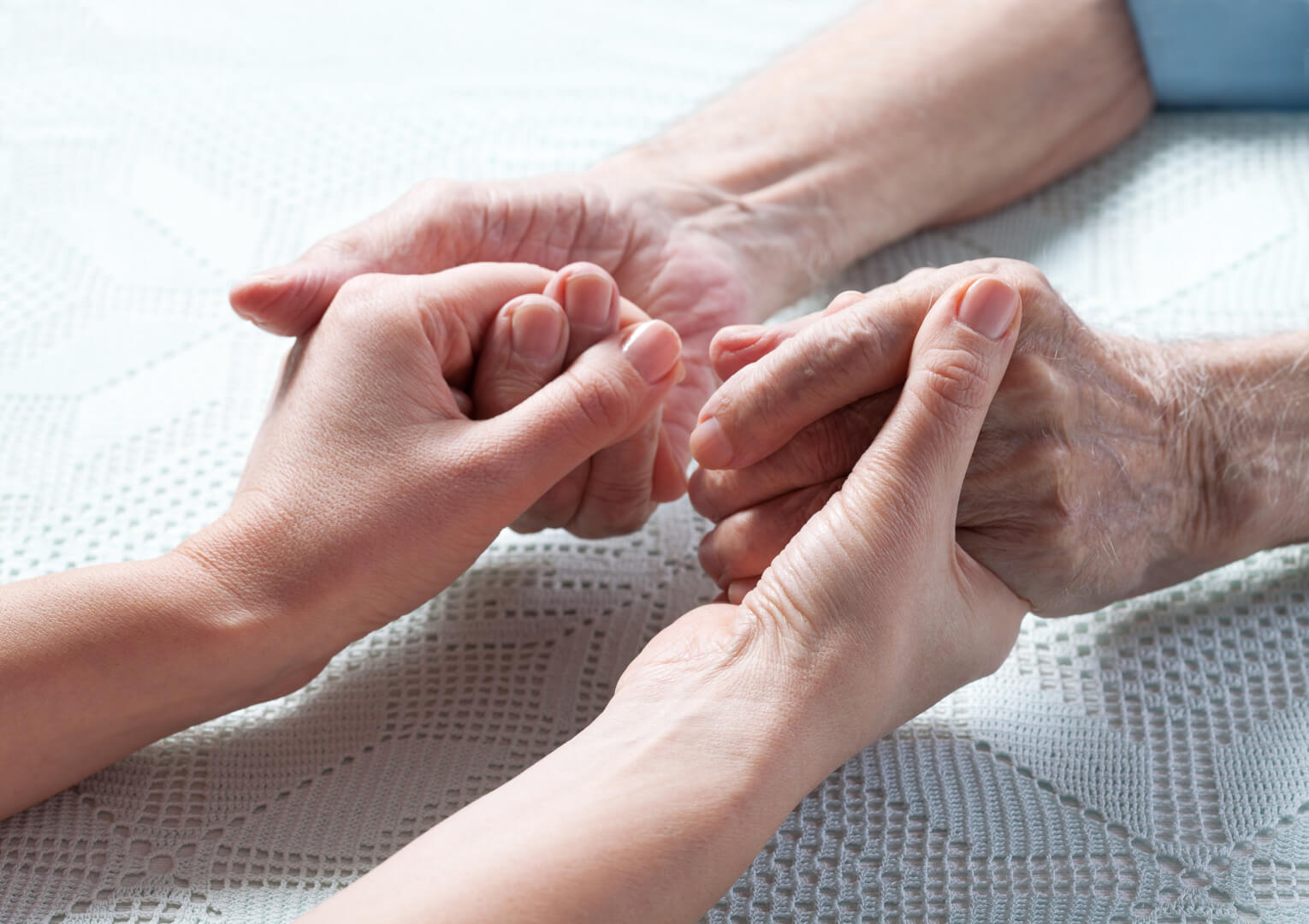 En la imagen se muestran unas manos de una persona mayor cogiendo fuerte las manos de una persona joven para ayudarle ante un problema.