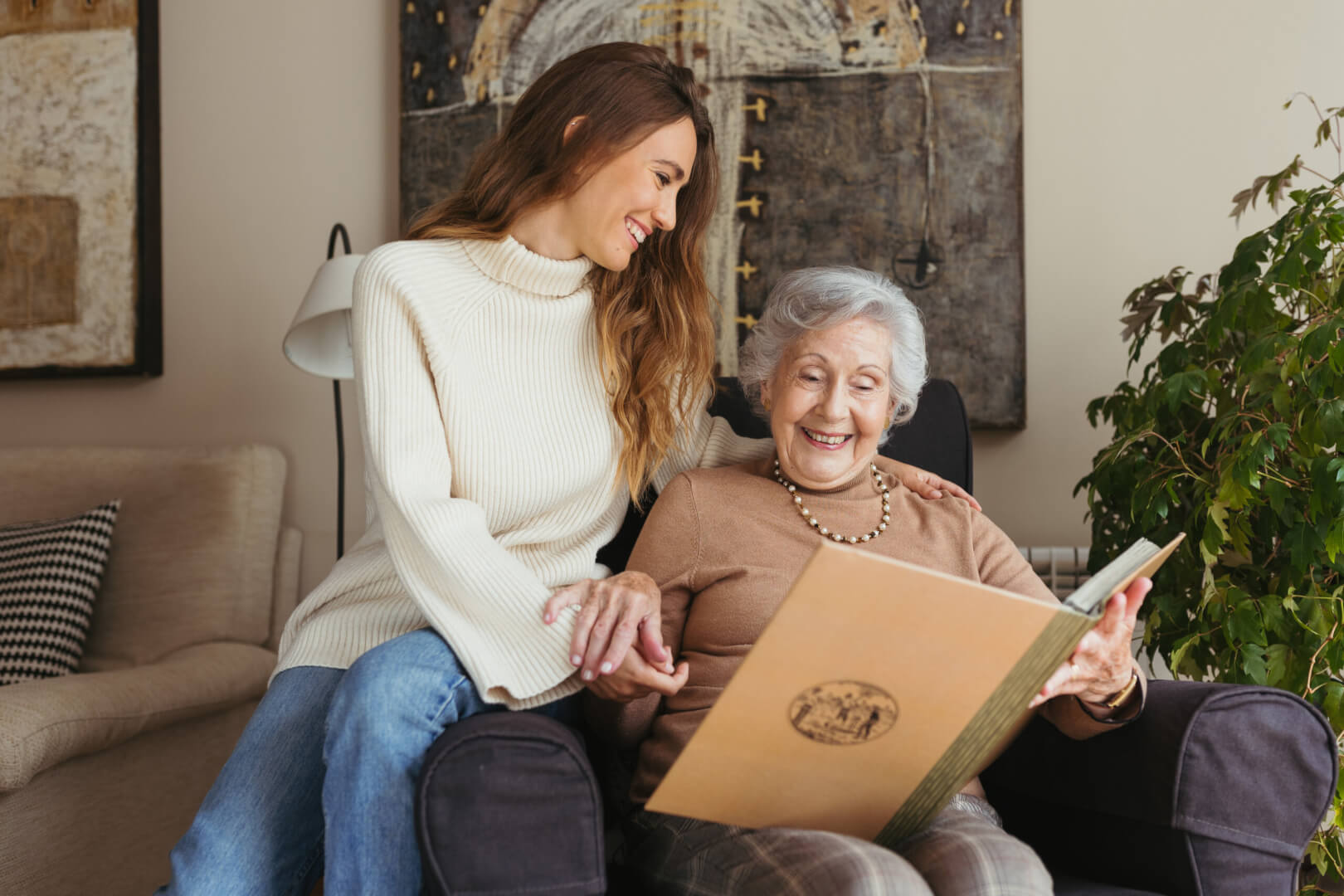Una trabajadora del hogar sonríe y comparte un bonito momento con una anciana mientras ven un álbum de fotos en una casa. 