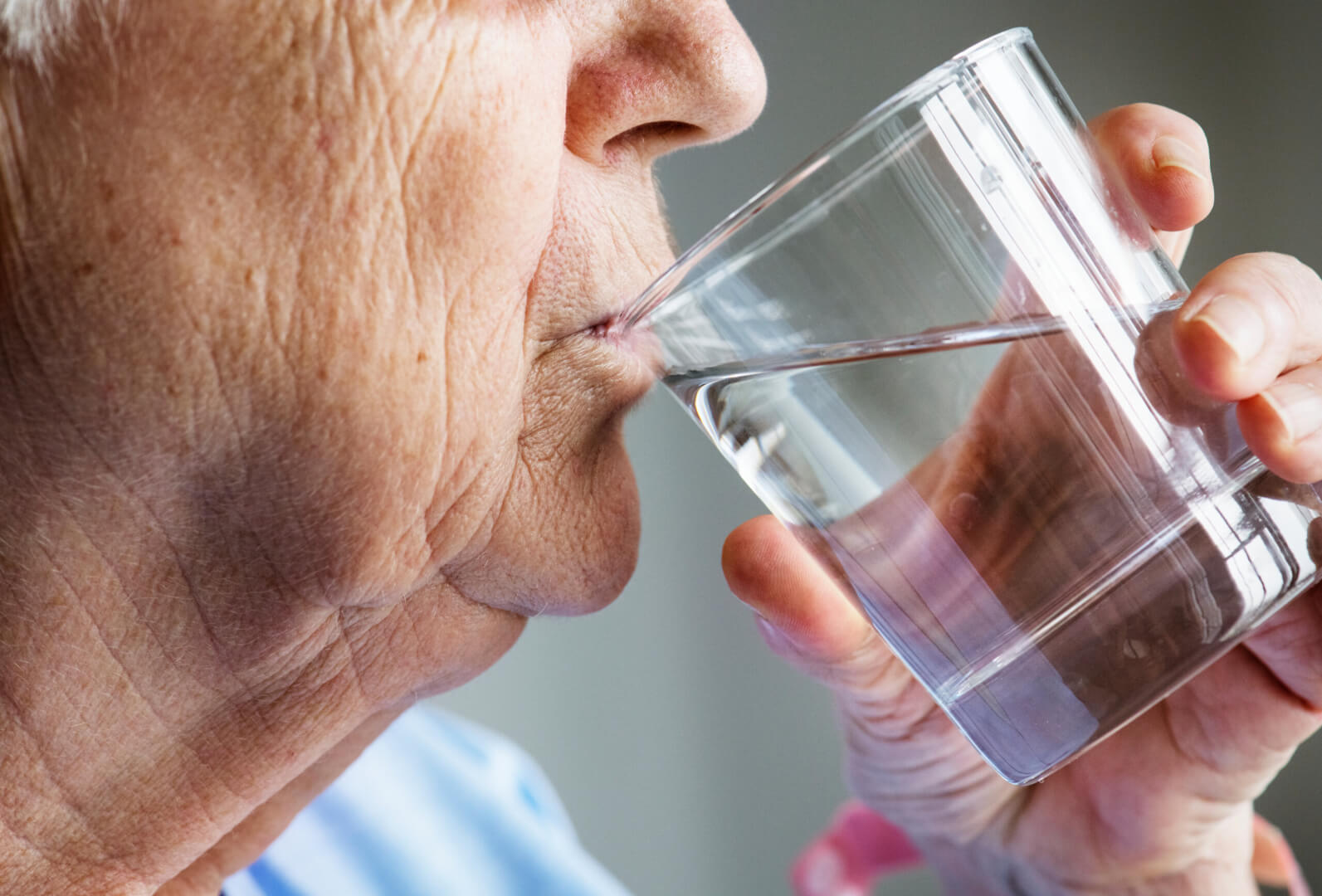 Un hombre mayor bebe un vaso de agua por la mañana en su casa para hidratarse y llevar una vida cardiosaludable.