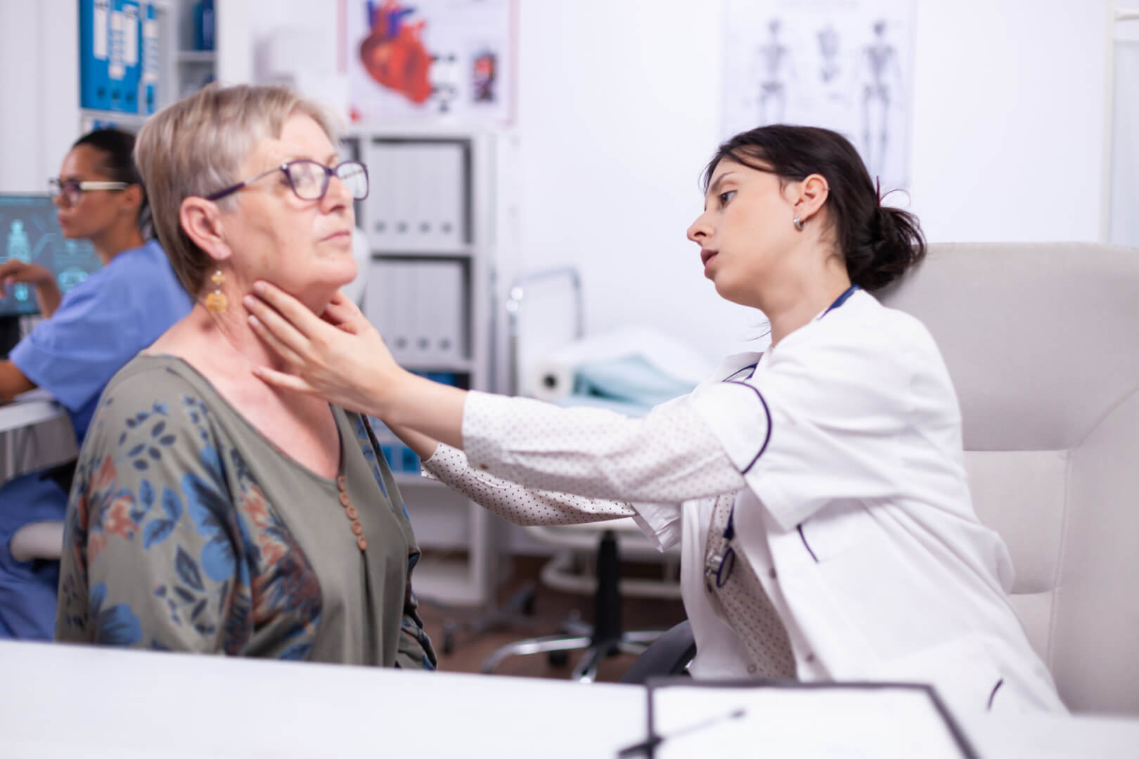 Una médico endocrina examina el cuello de una mujer mayor, donde está la tiroides.
