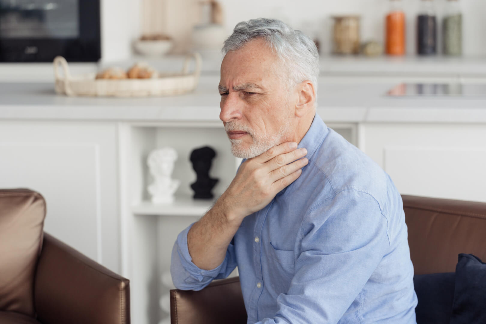 Un anciano se toca la glándula de la tiroides ante una molestia. 