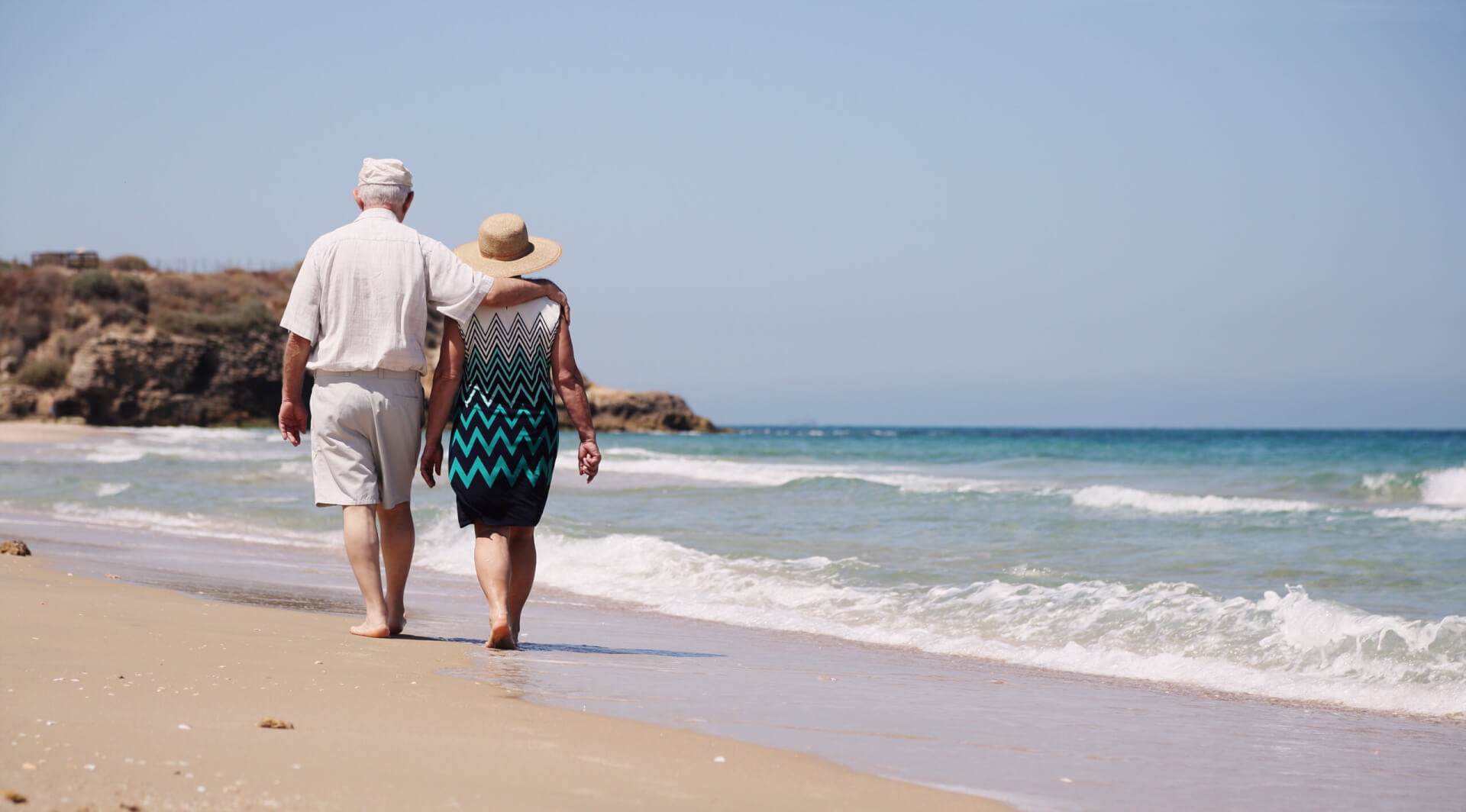 Una pareja de ancianos pasea por la orilla de la playa tranquilamente.