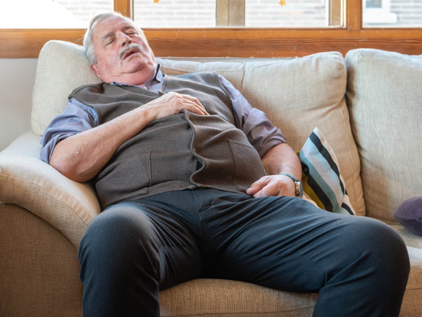 Un señor mayor se encuentra durmiendo en el sofá de su casa en pleno día.