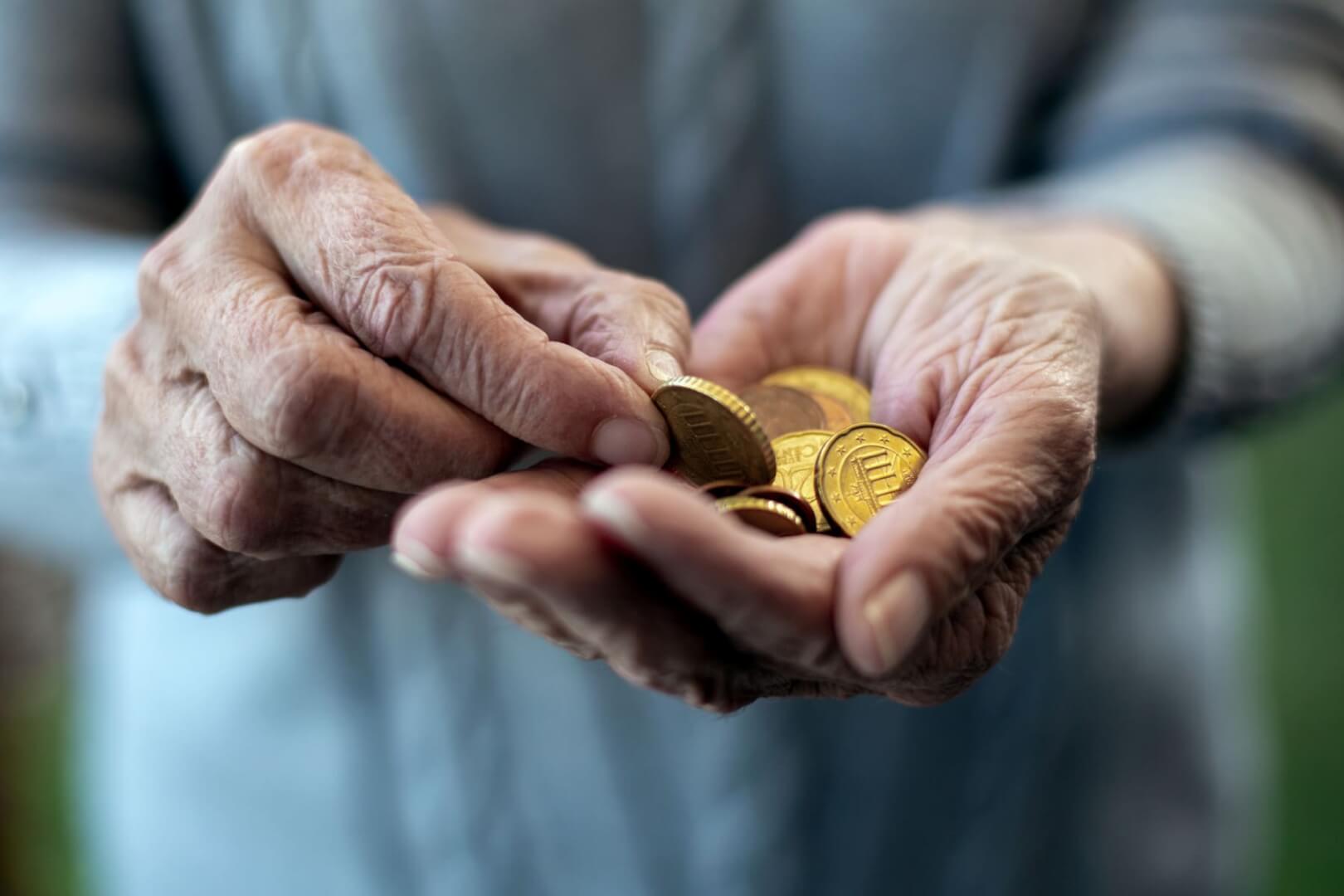 Un plano detalle de unas manos de un anciano con monedas. 