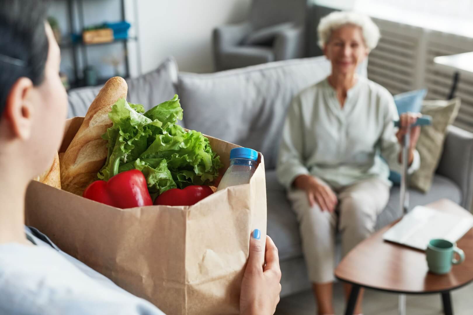 Una cuidadora acerca una bolsa con alimentos ricos en vitamina C como lechuga y pimientos a una anciana en su casa. 