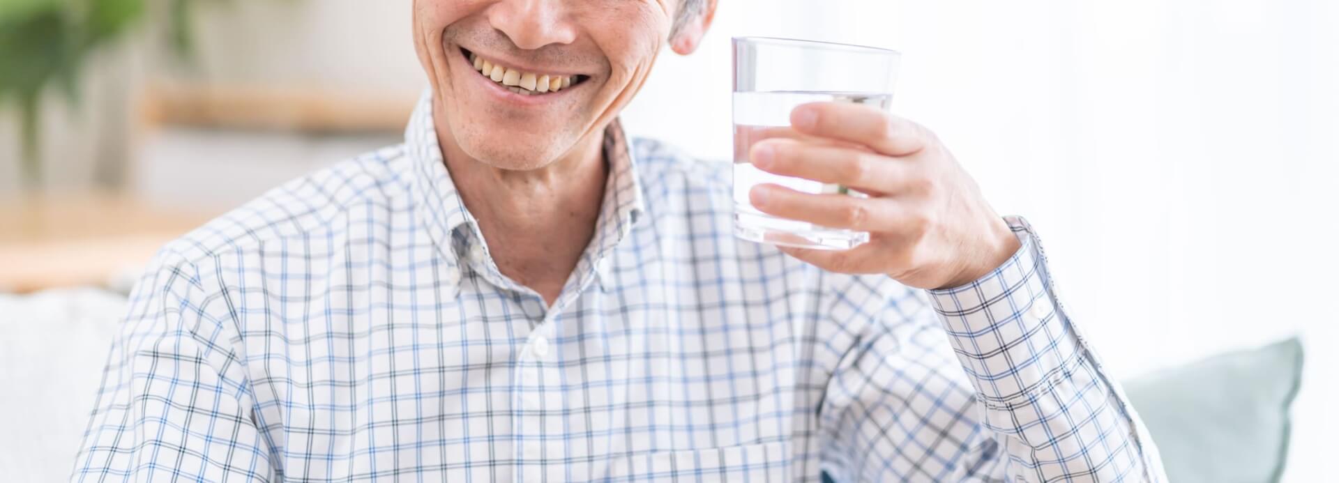 Hombre sonriendo con un vaso de agua y bicarbonato de sodio en la mano.