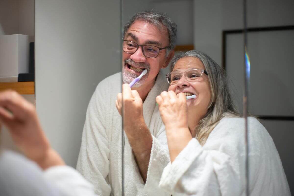 Dos ancianos se cepillan los dientes frente a un espejo. 